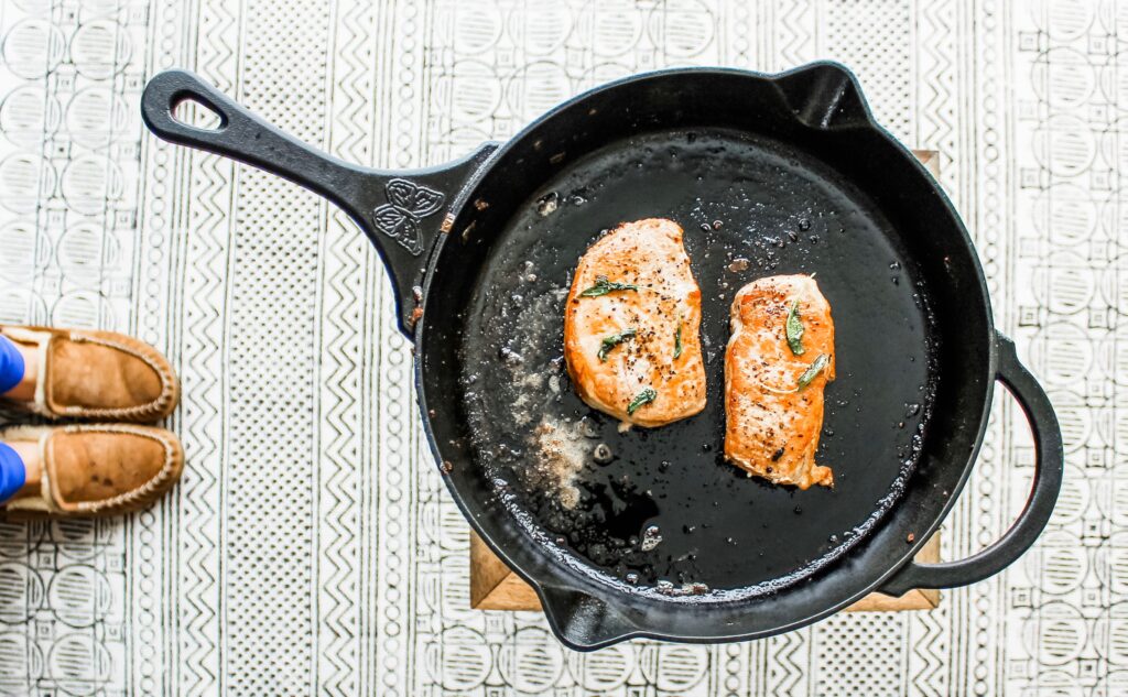 Pork chops searing in salted butter with fresh sage leaves.