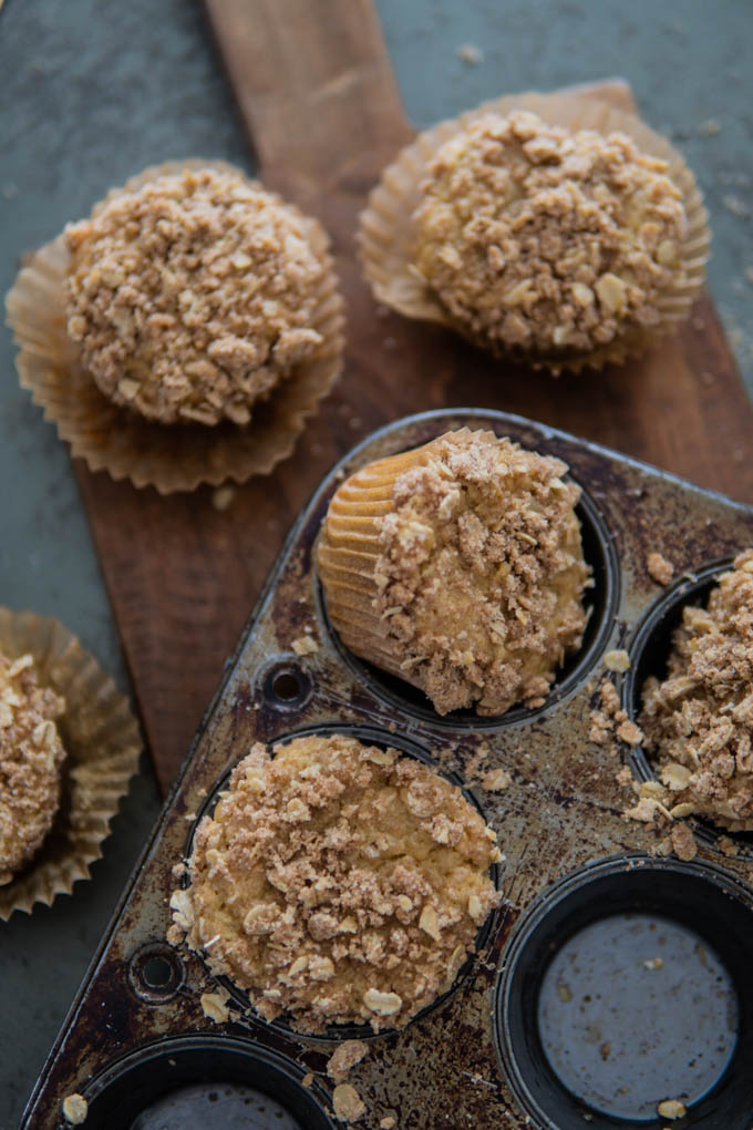 Ricotta banana muffins with oat crumb in a muffin tin and on a cutting board.