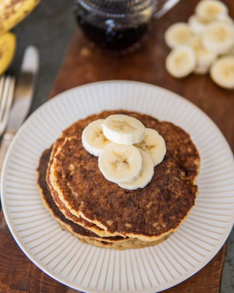 Small stack of Banana Oatmeal Pancakes with sliced bananas. 