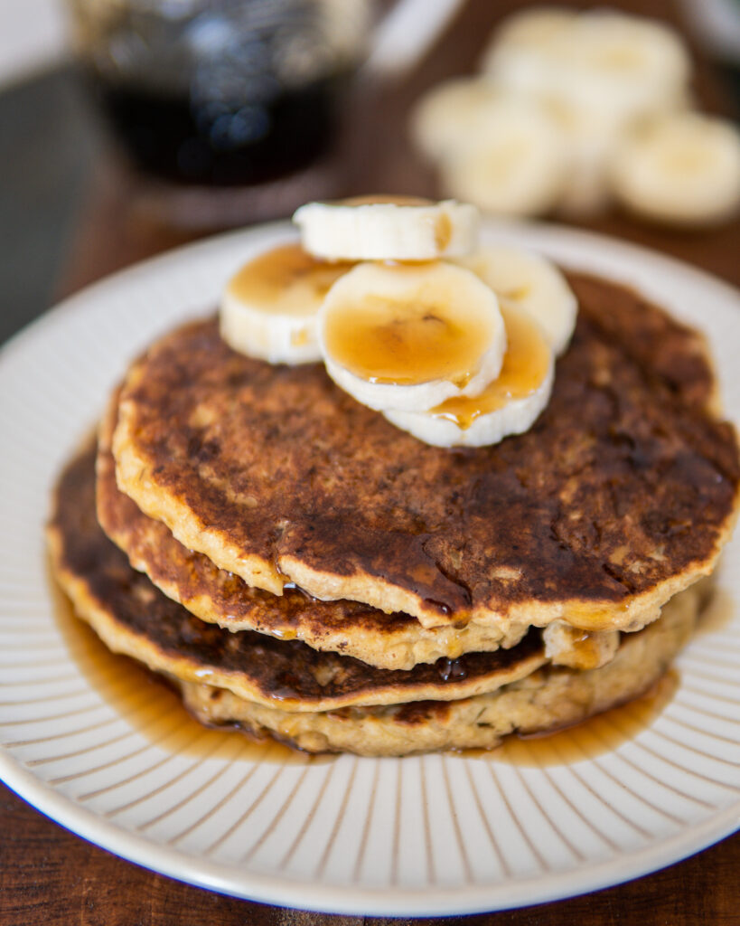 Small stack of Banana Oatmeal Pancakes with sliced bananas and maple syrup.