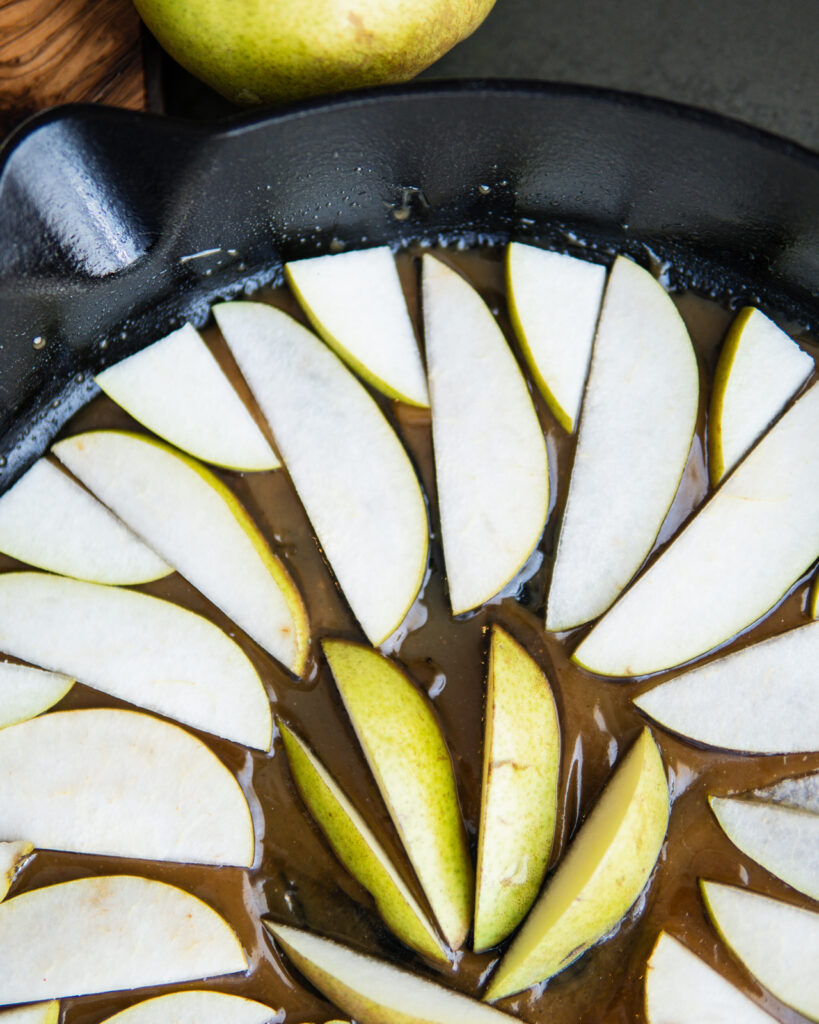 Pears laying in the skillet in the cardamom caramel.