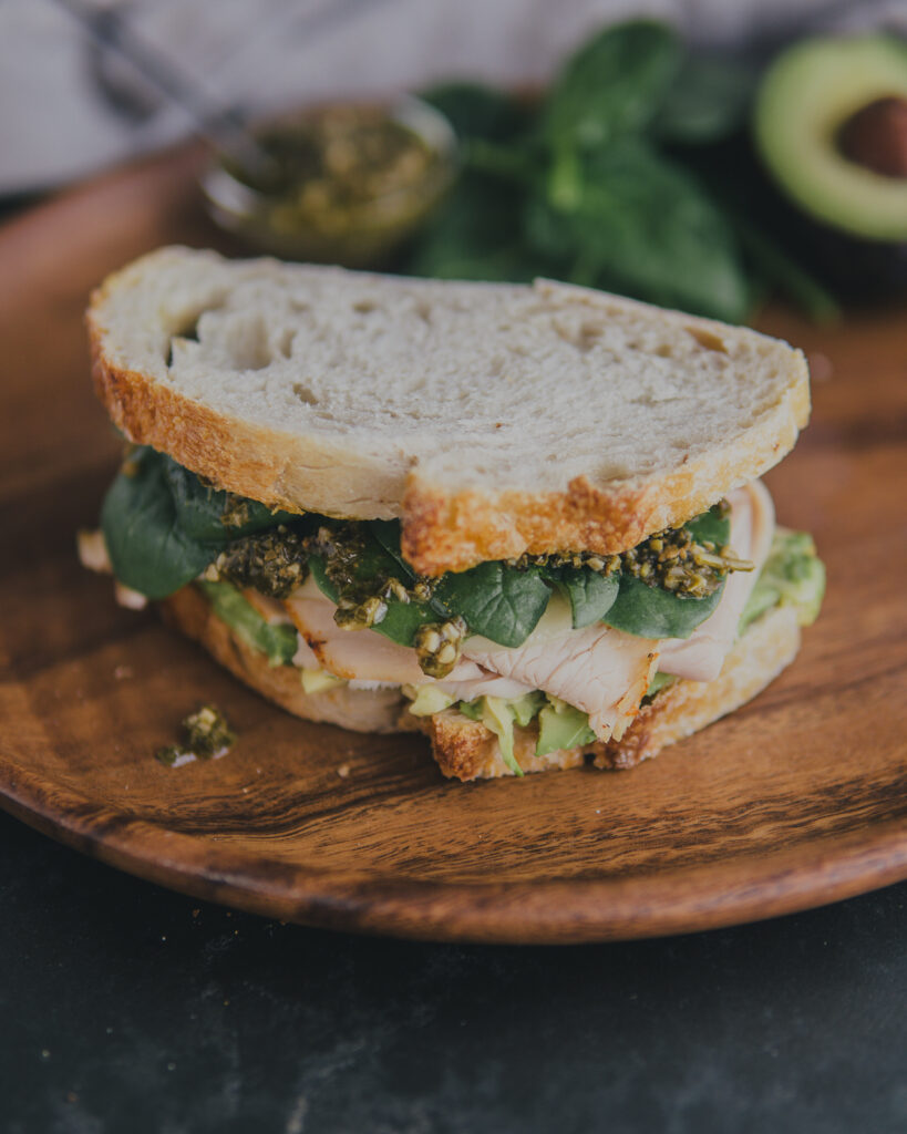 Pesto avocado turkey sandwich on a cutting board for serving.