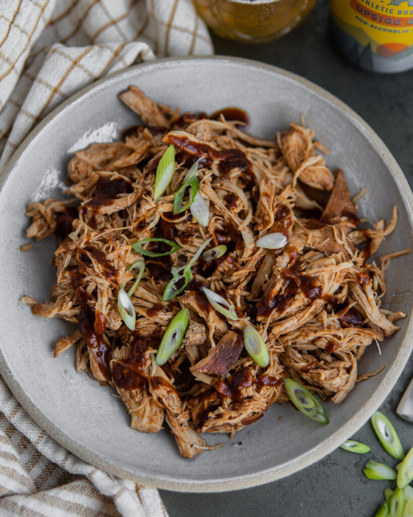 Beer & BBQ Pulled Chicken shredded in a bowl with BBQ sauce and green onions.
