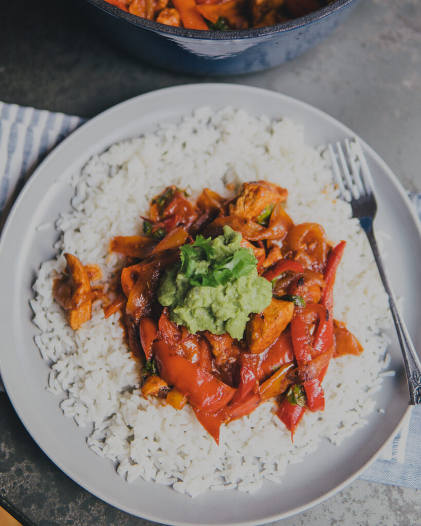 Finished plate of Dutch Oven Chipotle Chicken over a bed of rice topped with guacamole and cilantro.