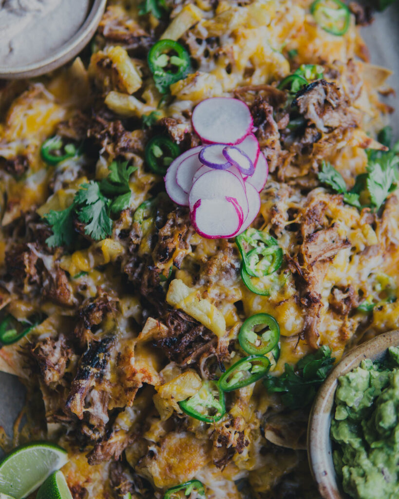 Close up on Sheet Pan Nachos with Carnitas & Roasted Pineapple with radish on top. 