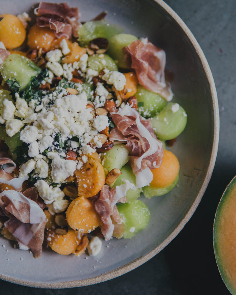 Melon & Prosciutto Salad in a bowl with crumbled feta on top. 