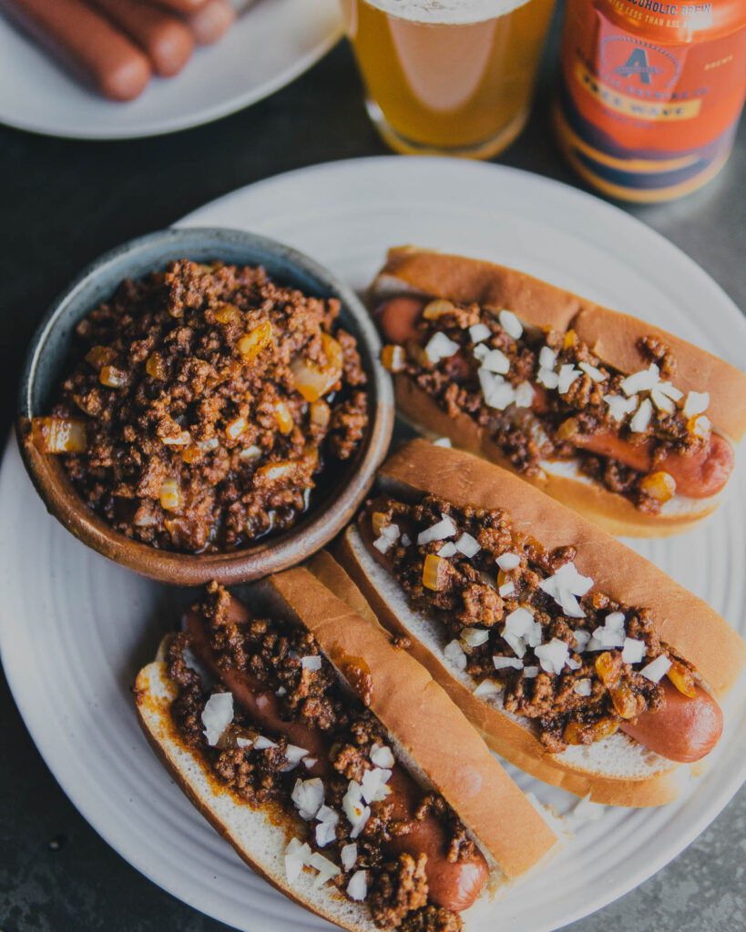 Three Free Wave Chili Dogs on a plate with a bowl of Athletic Brew chili on the side. 