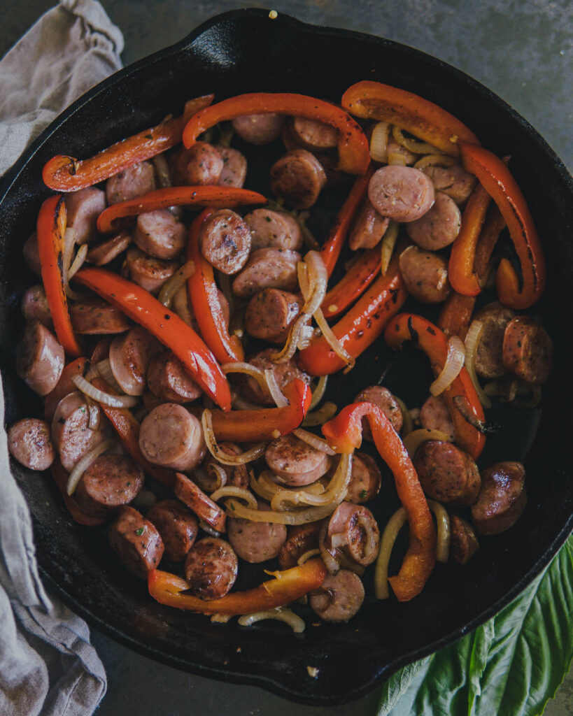 Italian sausage, onions and red bell peppers in a large cast iron pan. 