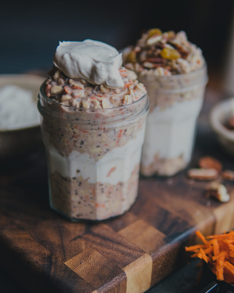 Carrot cake overnight oats in a jar topped with cream cheese mixture next to shredded carrots.