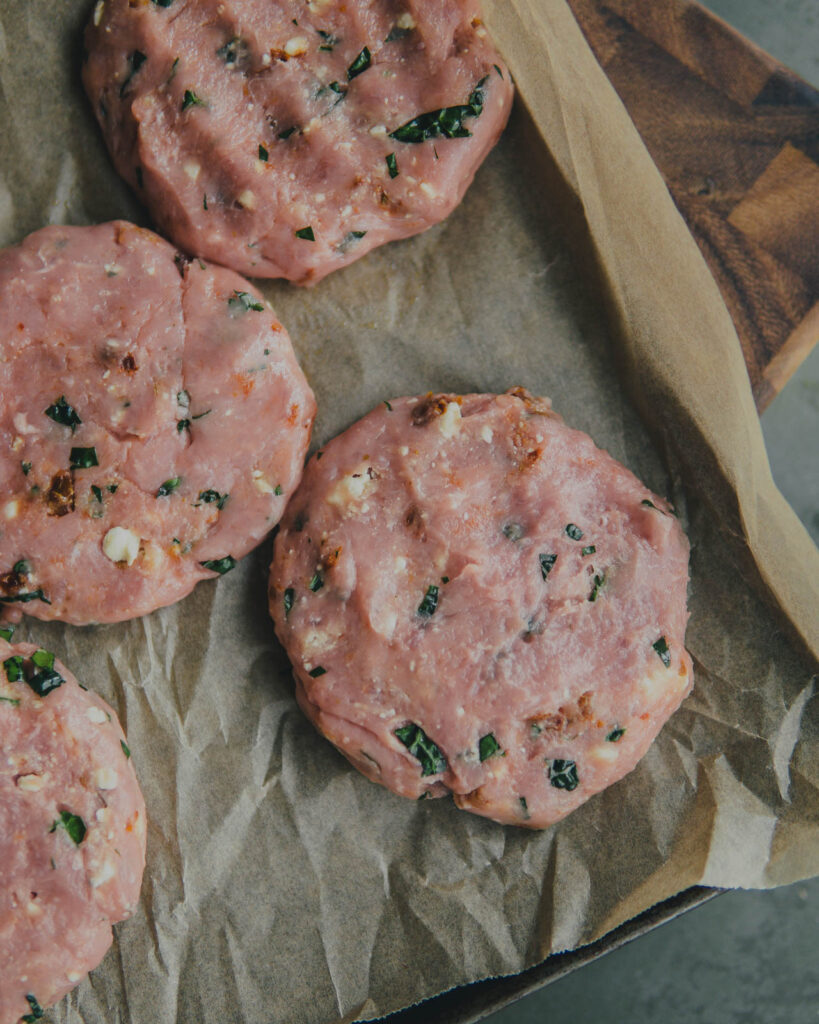 Raw turkey burgers on a parchment-lined baking sheet.