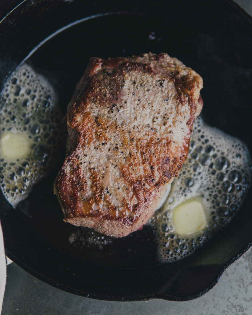 Tri-tip steak searing with salted butter in a cast iron pan. 