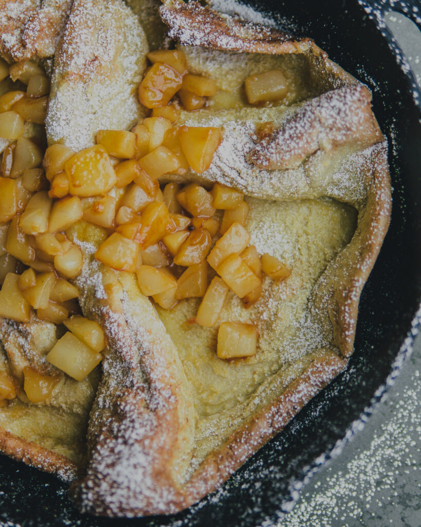 Closeup of Spiced Dutch Baby topped with apple cider pears and powdered sugar. 