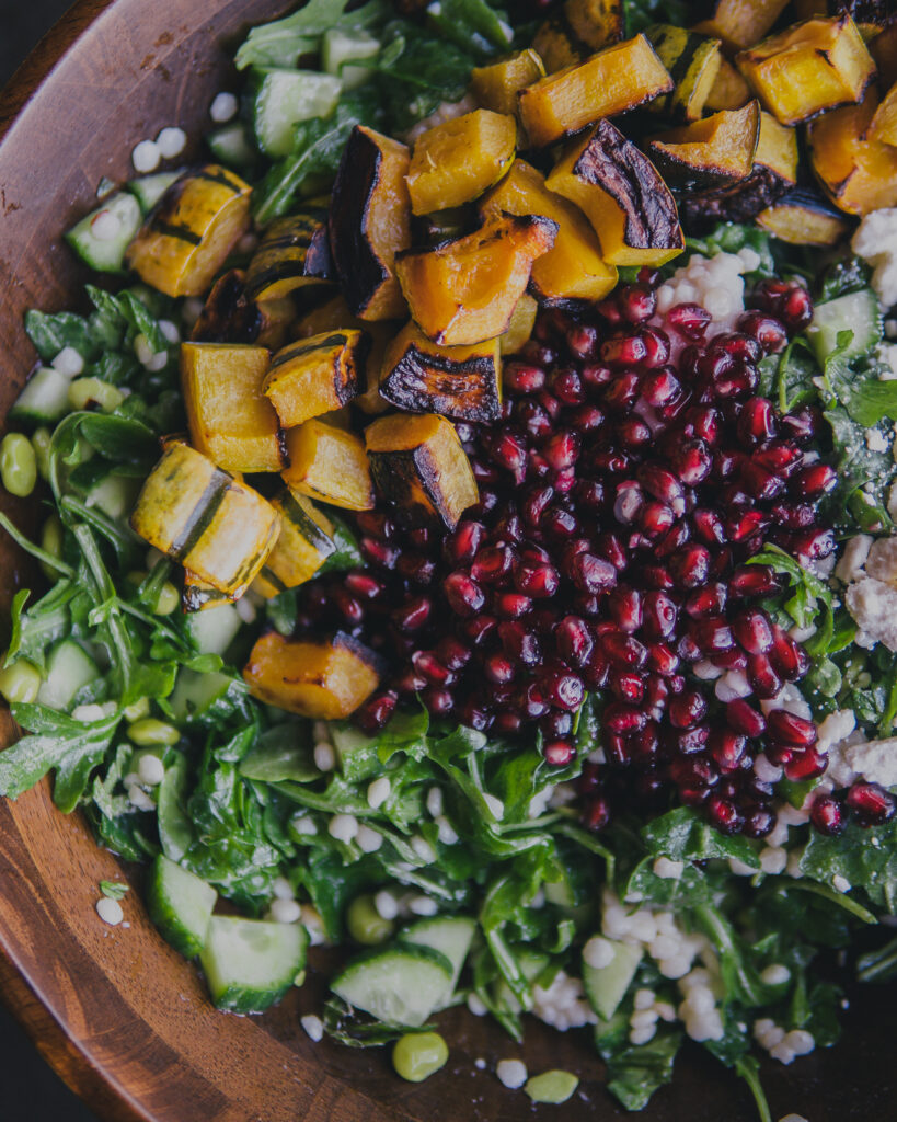 Closeup of winter couscous salad with pomegranate seeds and delicata squash. 