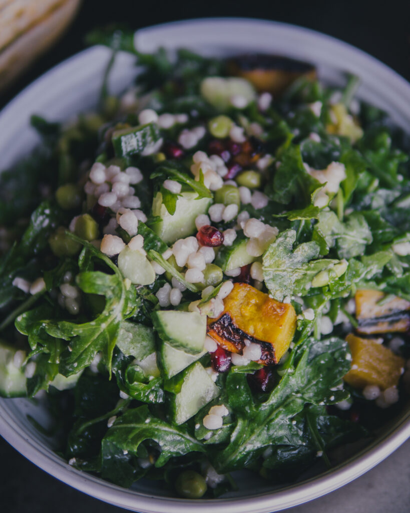 Winter couscous salad with arugula and cucumbers up close in a serving bowl. 